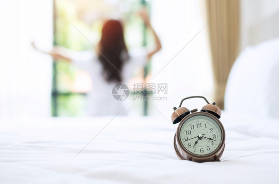 休息清晨时钟关紧闹其背景是幸福的女士醒来后在床上拉长年轻成女举起双臂期待着窗清新放松有美好的一天概念睡觉拉紧图片