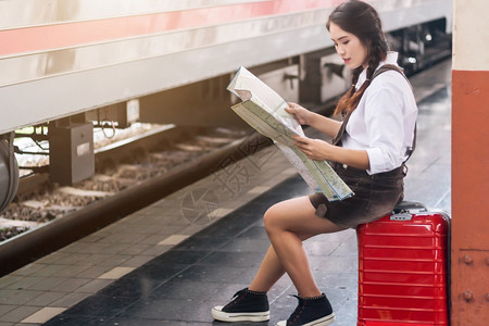 独自的母亲旅游在火车站行中用红色手提箱看豪来日旅行概念亚洲孕妇游客等待坐在长凳上着的亚洲孕妇在火车站旅行时观看该图片