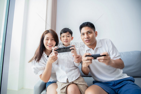 技术亚洲家庭一起玩电脑控制台游戏愉快的亚裔家庭父亲和儿子拥有手掌控制器母亲在家为球员欢呼着屋木板图片