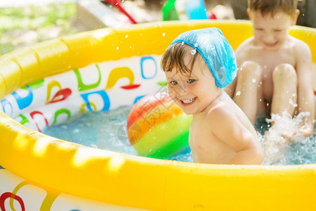 孩子们在游泳池里泼水和玩乐在游泳池里喷洒水玩得开心的孩童们洗澡时用黄色充气机动游泳池露天热暑夏日在户外游泳池洗澡笑黄色的男生图片