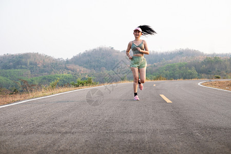 照片身穿运动服戴帽子慢跑健康生活方式概念在沥青路上奔跑的年轻笑着女跑步者脚丫子正在做图片