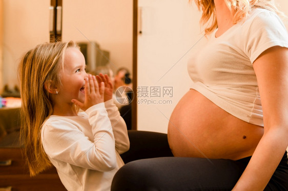 生活美丽的在家小女孩站孕妇母亲旁边站着等待小兄弟或妹出生而兴奋地等待着她出生新的图片