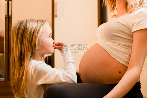 白种人在家的小女孩站孕妇母亲旁边站着等待小兄弟或妹出生而兴奋地等待着她出生活幸福图片