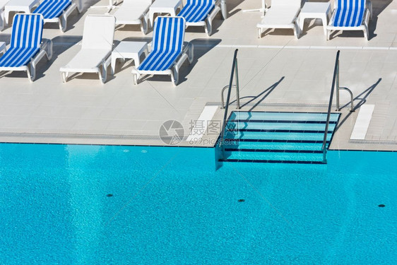 日光浴床池畔活动阳光明媚的一天带游泳池梯子的阳床和雨伞图片