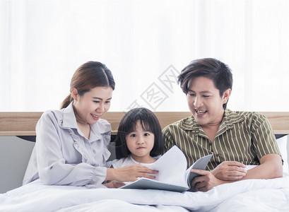 父亲关心请享用亚洲爸和妈在睡觉前给女儿看睡前的故事图片