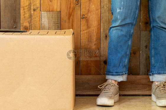 纸板移动箱在空房间里有木墙背景和复制空间搬进新公寓或房子概念复古设计腿运动鞋和牛仔裤空间用于文本纸板移动箱在空房间里有木墙背景和图片