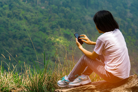 户外坐在岩石上看手机的女人图片