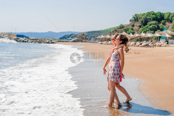 海岸线女两个快乐的孩朋友或姐妹站在海边的或看着水面微笑穿夏衣和太阳镜欢乐地笑着白种人图片