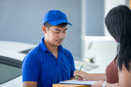 新冠命令亚洲送货服务人员身穿蓝色制服带帽子和搬运纸箱的亚洲送货服务人员在家中门前向女顾客提供在线购物和快递服务网上购物和快递服务图片