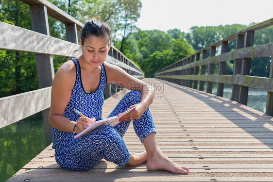 乡村的坐在自然界木桥上的年轻女作家记事本绿色图片