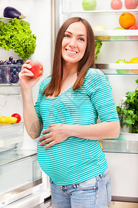 照片孕妇站在冰箱前手拿着桃子的蜜一顿饭腹部在室内图片