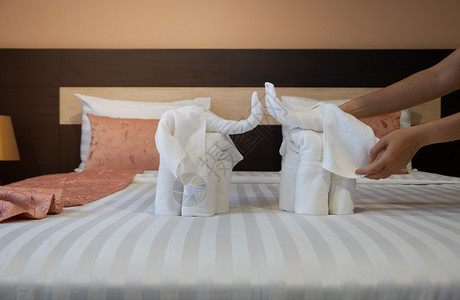 准备住宿美丽的近身手把白浴巾折叠起来像床单上的大象一样在床单上盖着白色浴巾图片