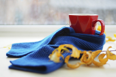 黄色的在雨季窗口背景下满脸咖啡的红色杯子桌上有蓝丝织围巾和黄秋叶旁边是雨天的窗口叶子疾病图片