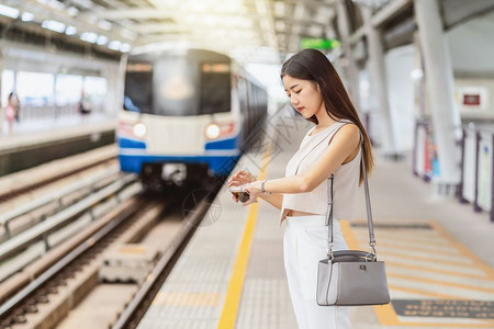 娱乐移动的上市通过智能移动电话和在地铁火车站手表日本钦朝韩生活方式通勤和运输概念看火车听音乐的亚洲年轻女乘客青运妇女利用智能手机图片