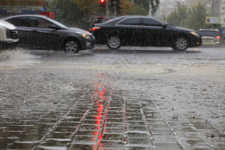 下雨滂沱人行横道路和上的暴风雨路过汽车的人行道上喷着由红色交通灯光照亮的横雨人行道上的大雨和沥青路被红交通灯照亮图片