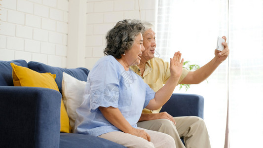 幸福手机亚洲年长的裔夫妇通过视频给家人打电话朋友在坐沙发上家客厅里时笑着开心地微老人和科技生活方式积极的老年人退休图片