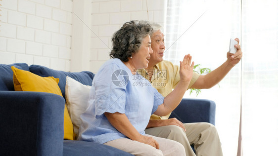 幸福手机亚洲年长的裔夫妇通过视频给家人打电话朋友在坐沙发上家客厅里时笑着开心地微老人和科技生活方式积极的老年人退休图片