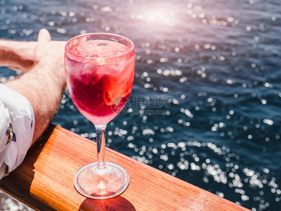 男人阳光美丽的酒杯有粉红鸡尾酒和冰块在海浪的背景下站在露天的甲板上侧观近距离的休闲概念带着粉红鸡尾酒和冰块旅行寒冷的图片