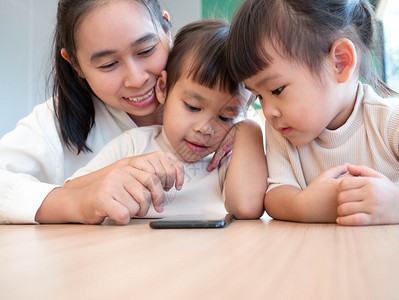 有趣的亚洲美丽年轻母亲及女儿在家用手机使应程序玩游戏或娱乐也于享受游戏或娱乐活动微笑在室内图片