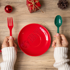 厨房圣诞节毛衣快乐妇女手握盘子叉和勺在木桌背景的Xmas派对和新年快乐概念图片