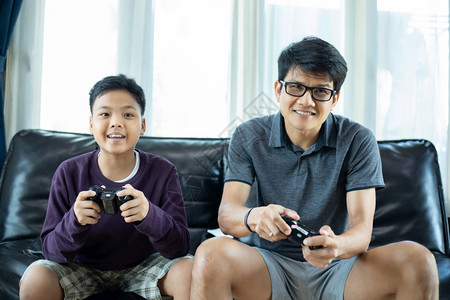 虚拟的年轻亚洲父亲和儿子在家中客厅玩电子游戏时享受与高跟棍一起玩电游戏兴奋地非常有趣玩起居室游戏男生图片