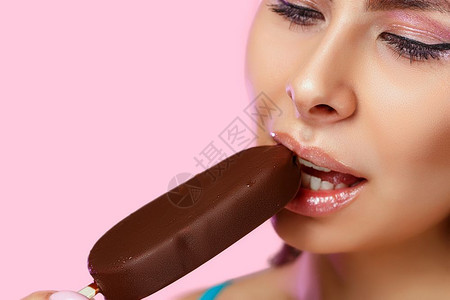 广告黑发一种个美丽的年轻女孩脸特写她用嘴在粉红色的孤立背景上咬着冰淇淋图片