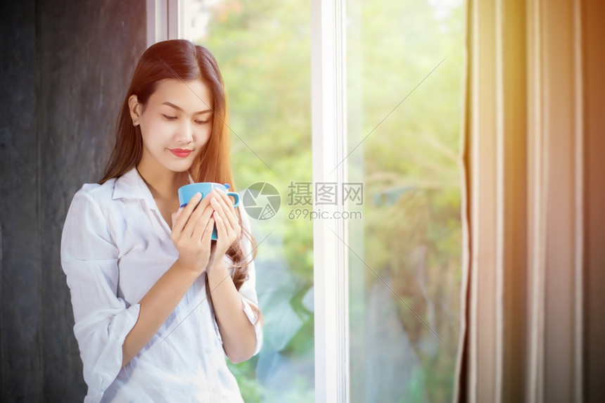 一名亚裔妇女站在咖啡杯上打开窗帘着当时她在家一天早上醒来后她站立在一旁女孩苏醒图片