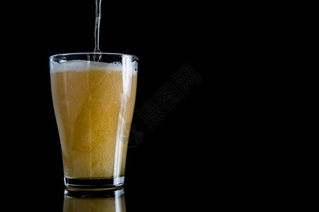 派对金子琥珀色黑背景泡沫啤酒倒在玻璃杯上黑背景泡沫啤酒倒在玻璃杯上黑色背景与复制空间图片