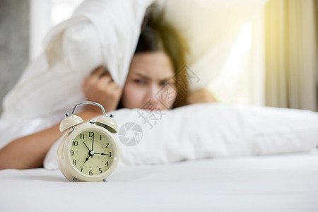 喜悦困唤醒亚洲女人讨厌早上一大醒来睡着的姑娘看闹钟试图躲在枕头下面藏起来图片