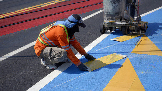 团队装修城市道路工人与带有热塑料喷雾路标识仪的公工人正在努力沥青路上油漆交通标志和自行车道街表面有铁轨交叉图片