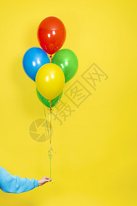 展示或者女手拿着一束五颜六色的气球派对或礼物概念绿色红黄和蓝气球手隔离在黄色背景上女手拿着一堆五颜六色的气球派对或礼物概念绿色黄图片
