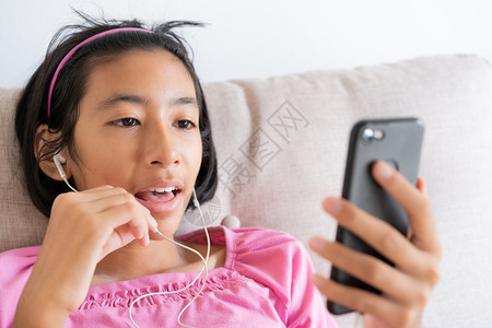 数字的亚洲女孩坐在家里客厅的沙发上在智能手机进行视频通话HappyAsia孩子脸上微笑用耳机聊天超越互联网生活方式和放松的概念尽图片