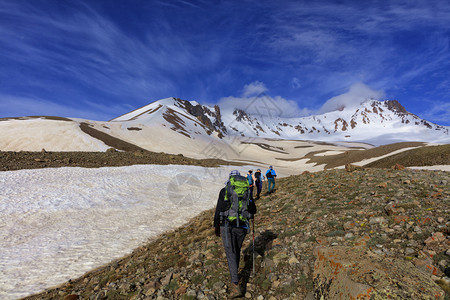 天空攀登一群背着包的游客在石坡上徒步前往土耳其的雪山埃尔西亚斯一群游客爬上山的石坡到雪峰旅行图片