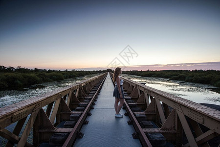 小路一位妇女走在座城市桥上看着湖边的夕阳风景一个暑假的妇女走在一座城市桥上看着湖边的日落风景青春期女士图片