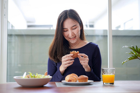 饮食喝美丽的年轻青女在家中健康生活方式早餐中吃健康沙拉后抱着并有一点吃的面包和一杯新鲜橙子汁的图片