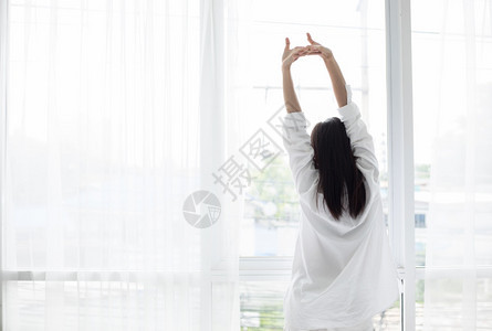 在床上醒来的亚裔女人完全休息早上打开窗帘呼吸新鲜空气早期的钟家图片