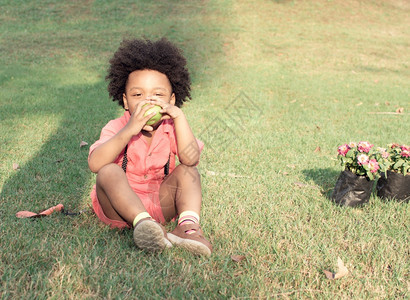 纯真快乐的一个穿粉红衬衫的非洲小男孩在后院玩耍吃苹果乐趣图片