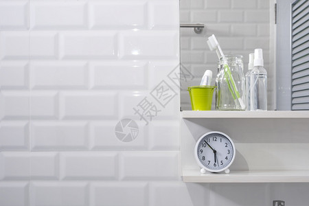 时间酒精早晨玻璃瓶中的牙刷小绿色桶中的牙膏在现代浴室的白色瓷砖墙上贴着时钟和镜子的洗手液喷雾以及个人配件图片