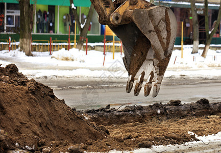 旧挖土机桶上的牙齿在土沟徘徊同时在冬季修补城市街道的公路在冬季用挖土机修复道路在冬季使用挖土机修理道路铺沥青挖掘机磨损图片