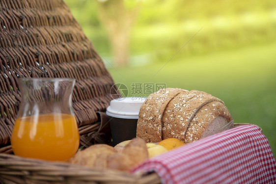 新鲜的快乐户外面包和橙汁在新鲜绿公园的木野餐篮子上甜有机健康饮料与咖啡杯及羊角面包糕饼烤鸡肉篮子公园中吃得非常美味图片