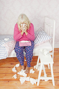 粉色的生病女士有粉色睡衣和组织坐在床上吹她的鼻子消息遭受图片