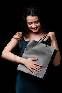 商业的身着深绿裙子的年轻美女手里拿着黑纸购物袋在色孤立的背景下被困在她手上女孩星期五图片