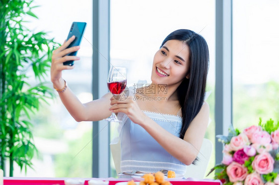 淑女情人节概念欢乐的自喜笑的亚洲年轻女坐在餐桌食物与酒杯在餐厅背景中快乐的香槟酒图片