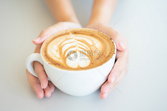 木制的茶杯子女人手拿着白咖啡杯是木桌上的一张拿铁咖啡桌复古风格从顶部看到奶泡的沫图片