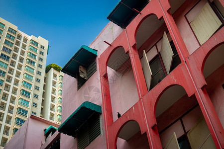 后面的旧红粉色建筑在明亮的蓝天有一座巨大高的现代公用寓正面墙新的图片