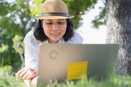 人们一种阳光亚洲女使用笔记本电脑工作躺在公共园绿草地上生活方式商业概念图片