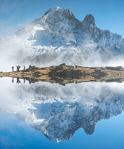 背包镜子反射山峰映在阿尔卑斯山脉的水面上一些人徒步登山图片