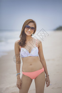 身着比基尼穿的美丽亚洲年轻女在海边滩面带笑脸时尚夏天快乐图片