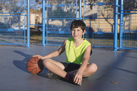无袖的合身竞技坐在球场上的年轻篮运动员穿着无黄色袖子图片