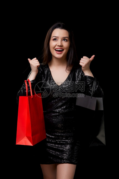 一位身穿黑色连衣裙的年轻女子对礼物感到满意在黑色孤立的背景下买黑色和红的袋子给予女孩星期五图片